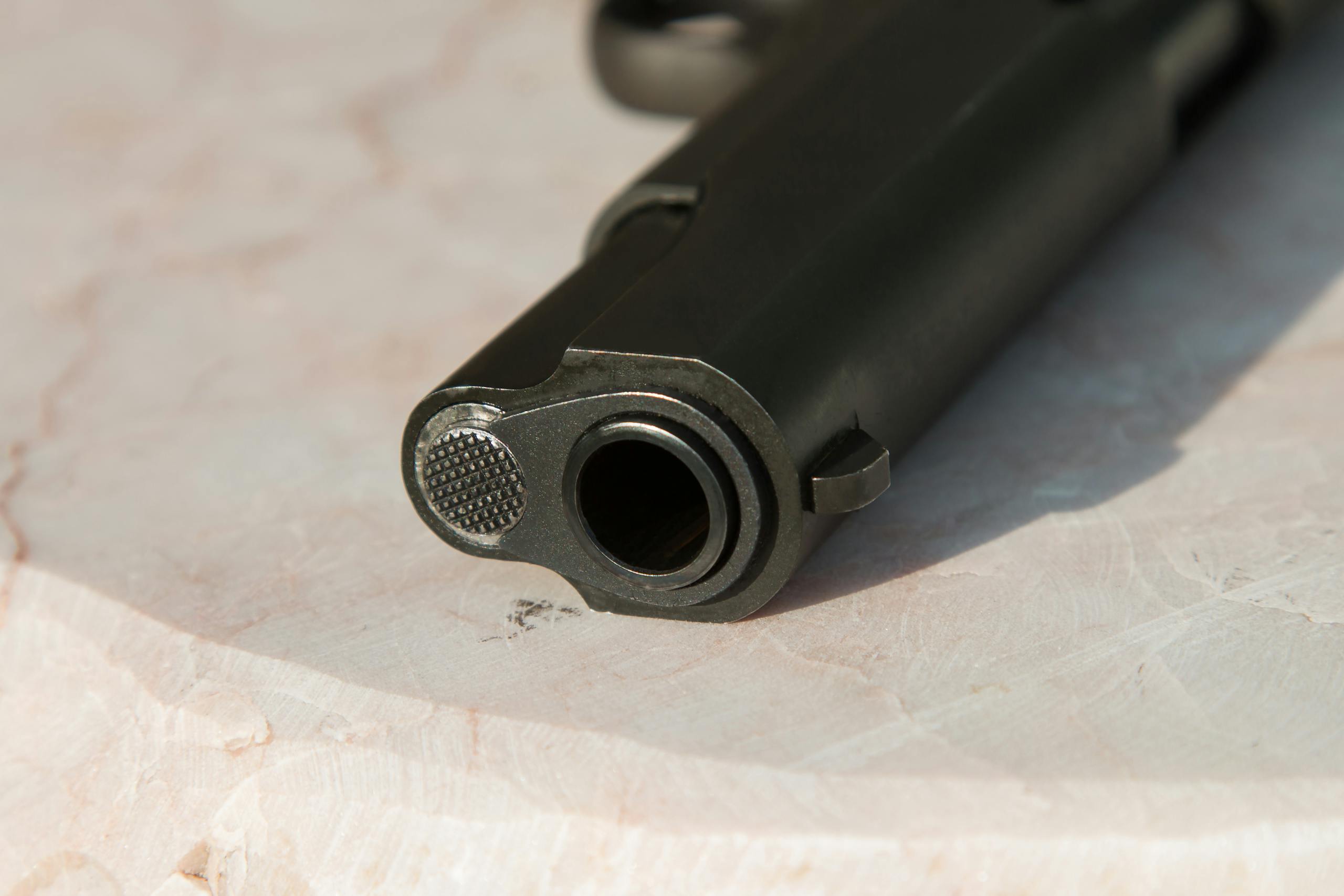 Detailed close-up of a gun barrel resting on a marble surface, highlighting the metal texture.
